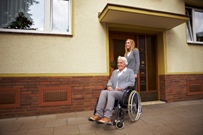 Woman in wheelchair with carer outside flat